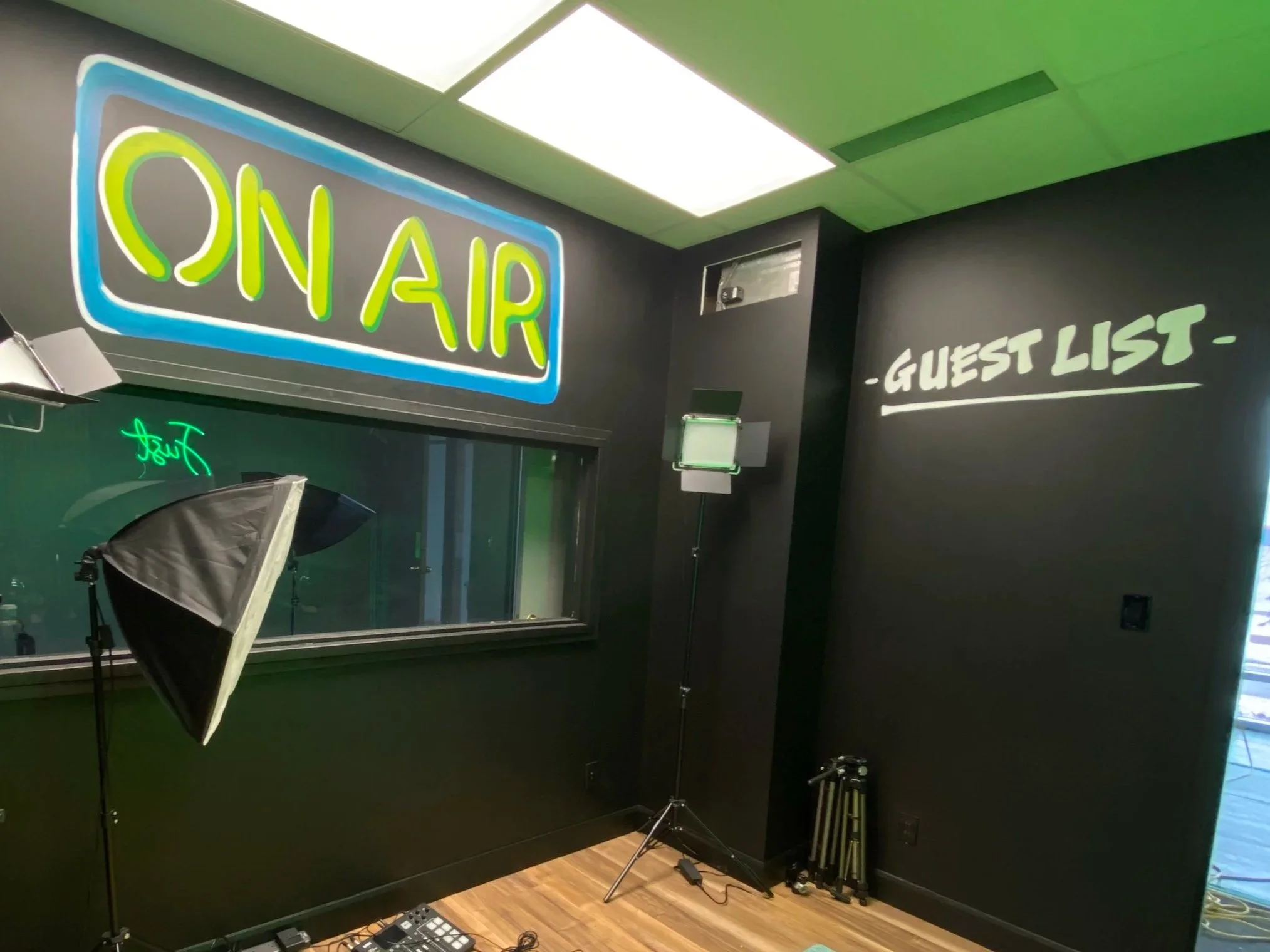 Painted words to look like neon sign that says "On Air" in Edmonton podcast space with Guest list written in white on black walls