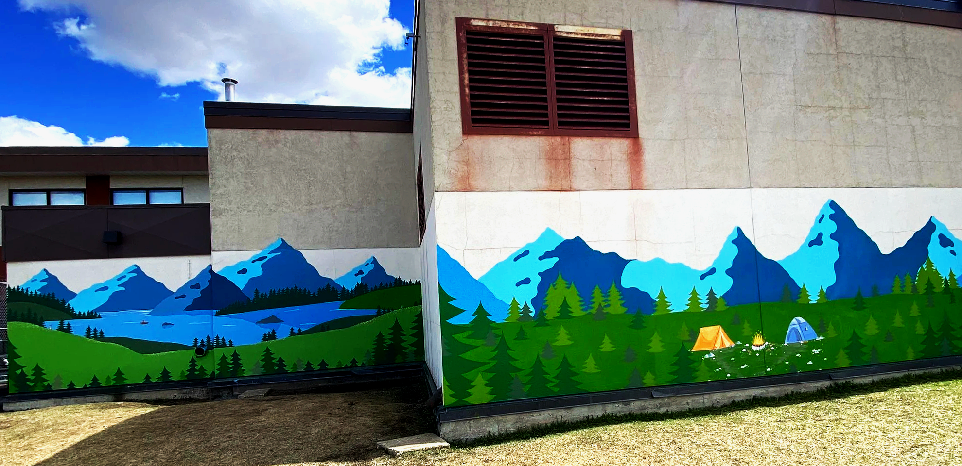Wall mural of mountains, trees, a lake with boats, scattered tents, and a campfire, painted on the side of a building featured on the back of Rimbey Elementary School hand painted by Carly Marie Murals.