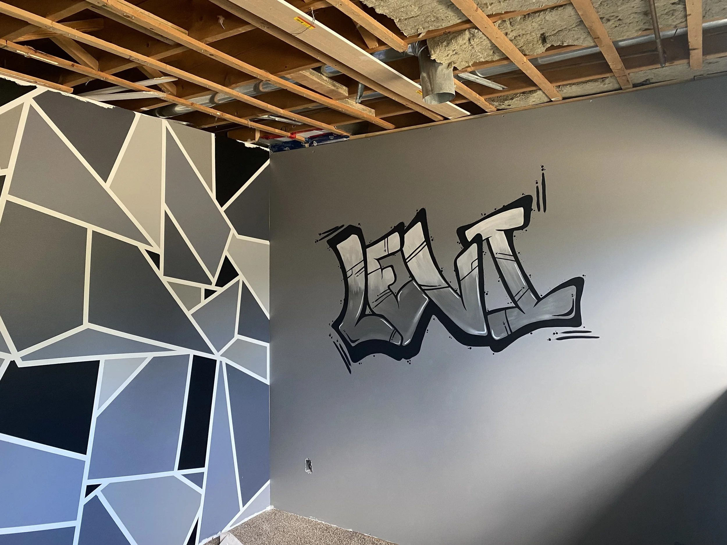 Partially finished interior wall with geometric black and white paint design next to plain gray wall with graffiti art. Painting done by Edmonton, AB artist Carly Marie Murals