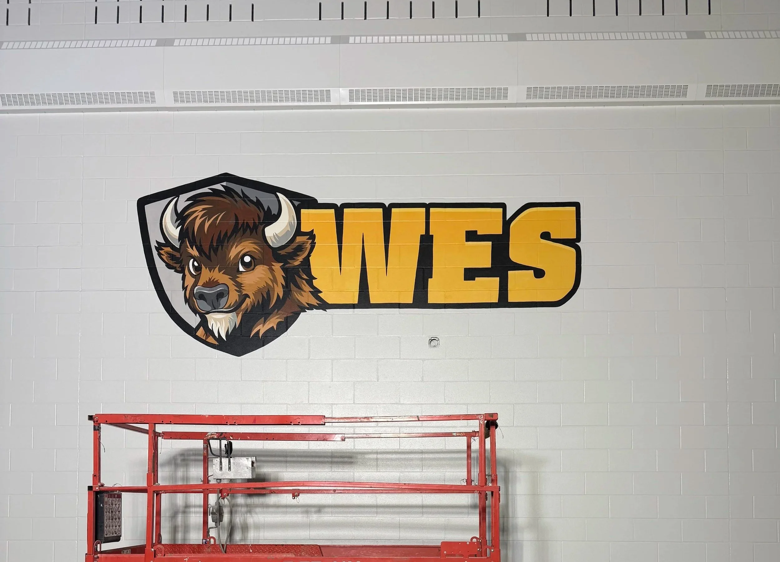 Large Wainwright Elementary School WES buffalo logo mural hand-painted on the new school gym wall by Carly Marie Murals in Wainwright, Alberta
