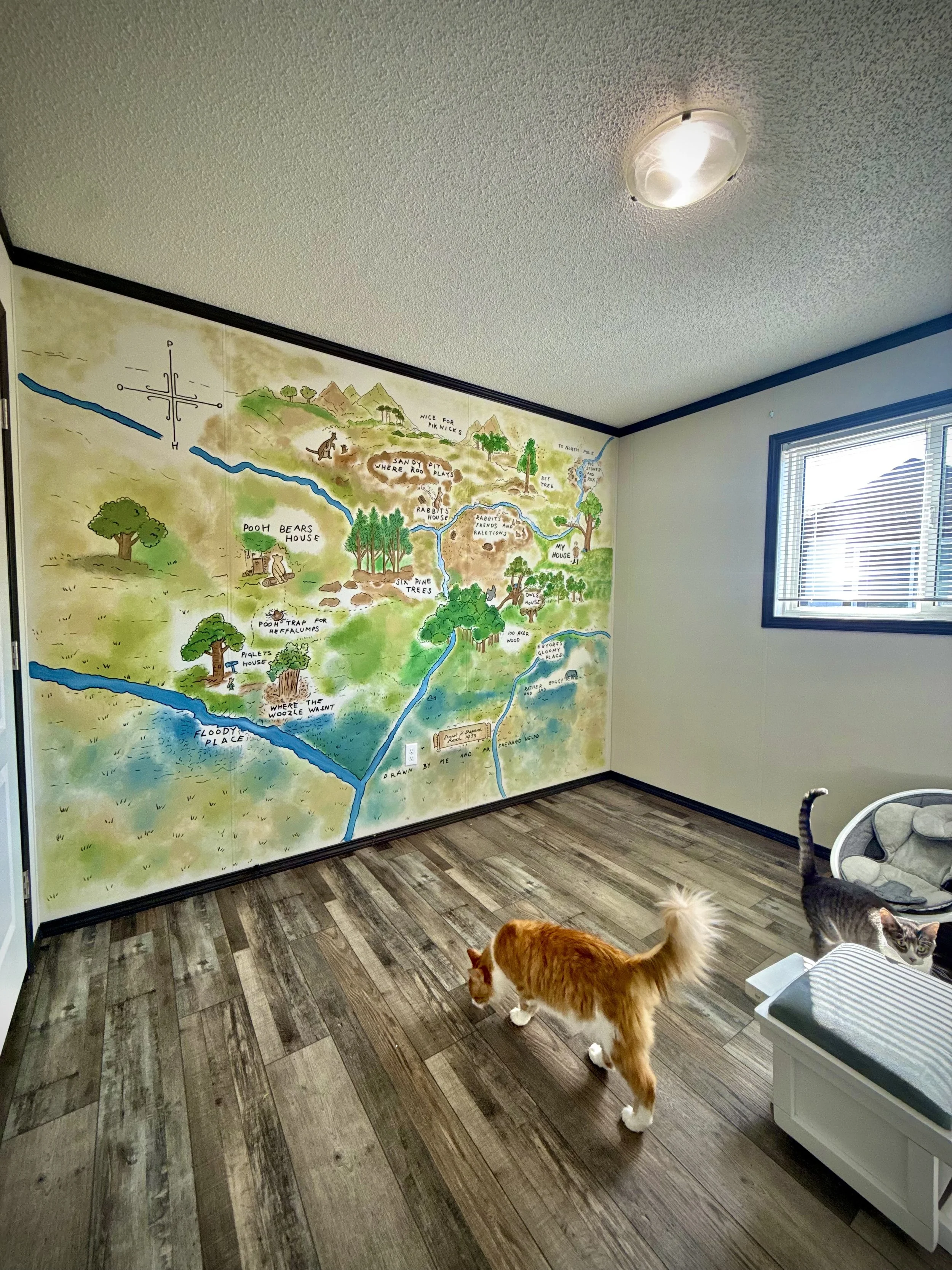 A kids nursery mural featuring a colorful illustrated map of the Hundred Acre Wood on the wall of baby room by Edmonton, AB artist Carly Marie Murals