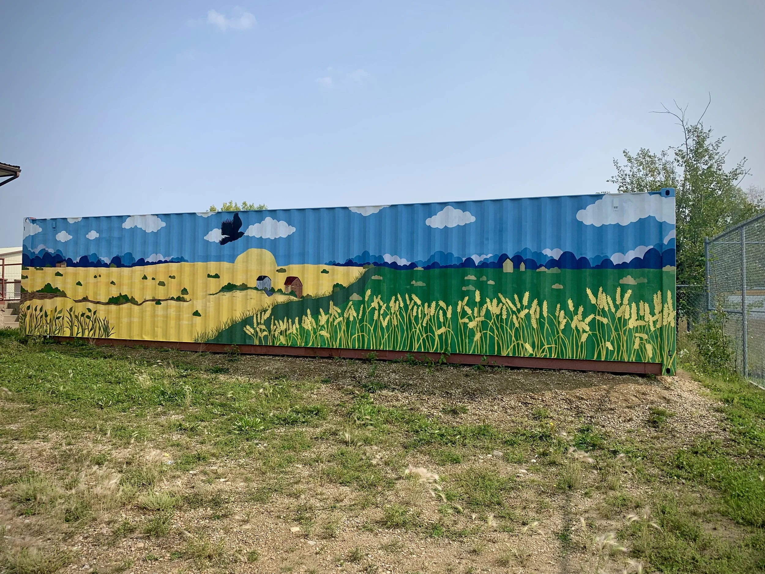 Hand painted mural of blue skies and buildings with grass and wheat land on shipping containers in west country outreach school