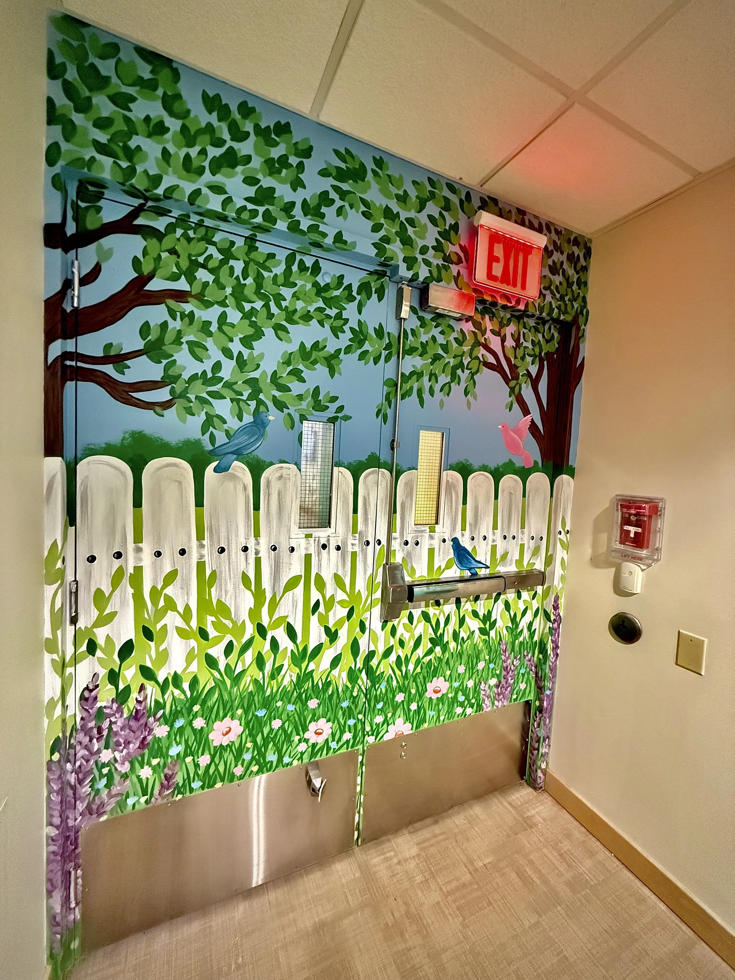 Colorful mural depicting a garden scene with green trees, grass, flowers, and birds, painted on a door in an indoor setting.