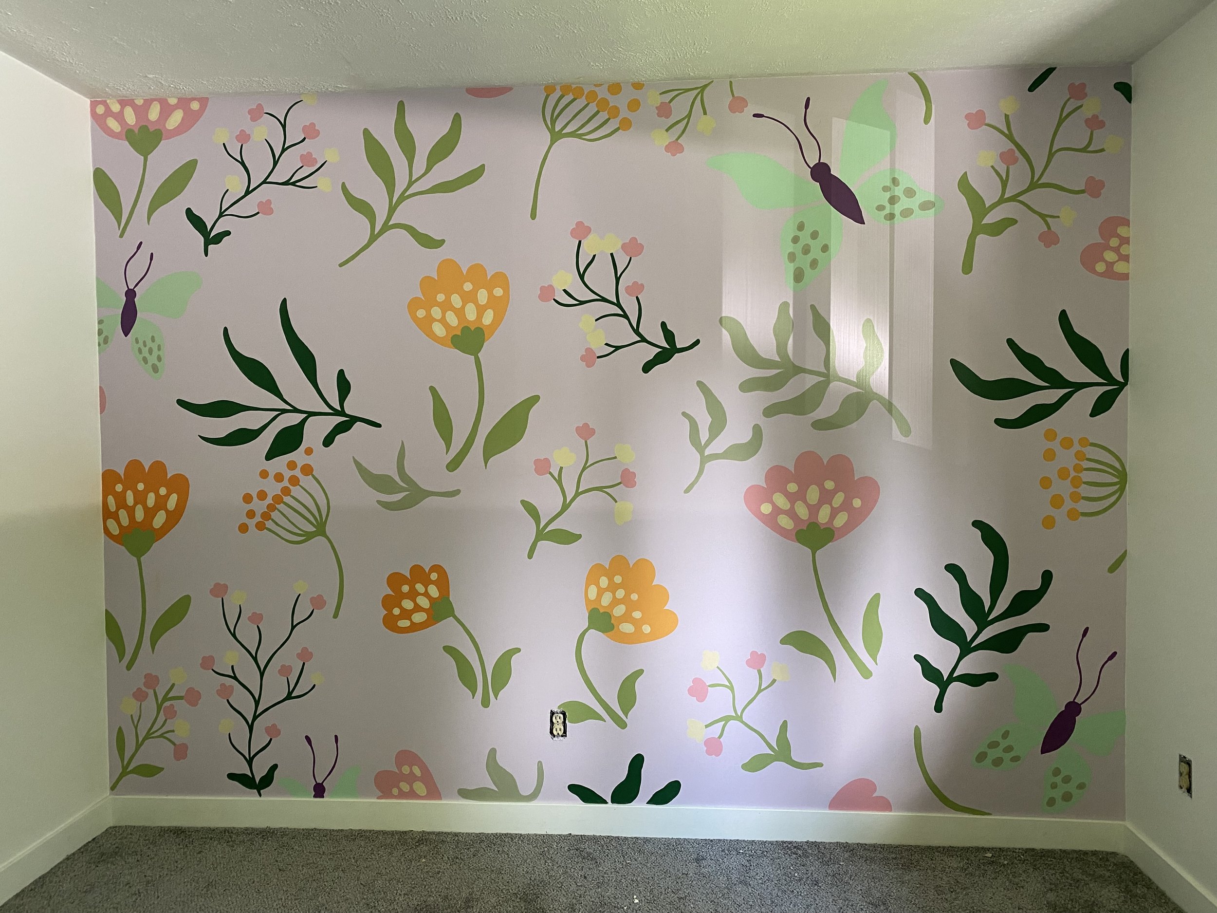 A kids nursery room with walls painted with a colorful floral and butterfly mural. The mural includes pink, orange, green, and purple hues with various flowers and butterflies spreading across the wall  by Edmonton, AB artist Carly Marie Murals