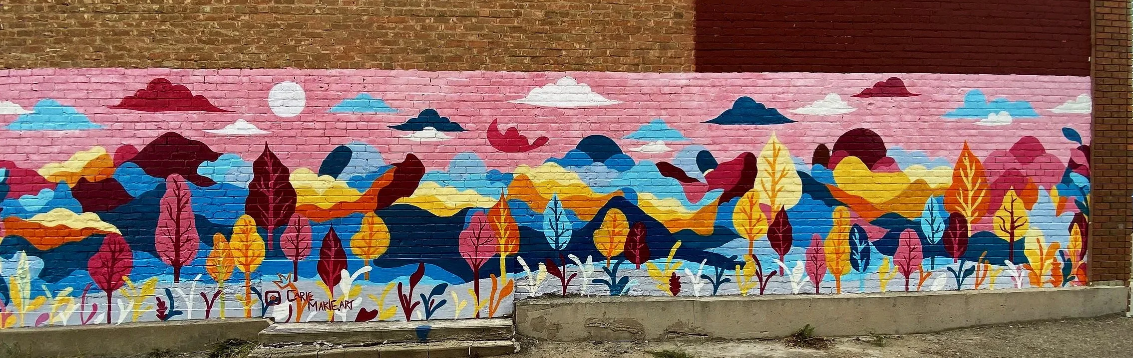 Colorful mural of trees and mountains on a brick wall with a pink sky and clouds