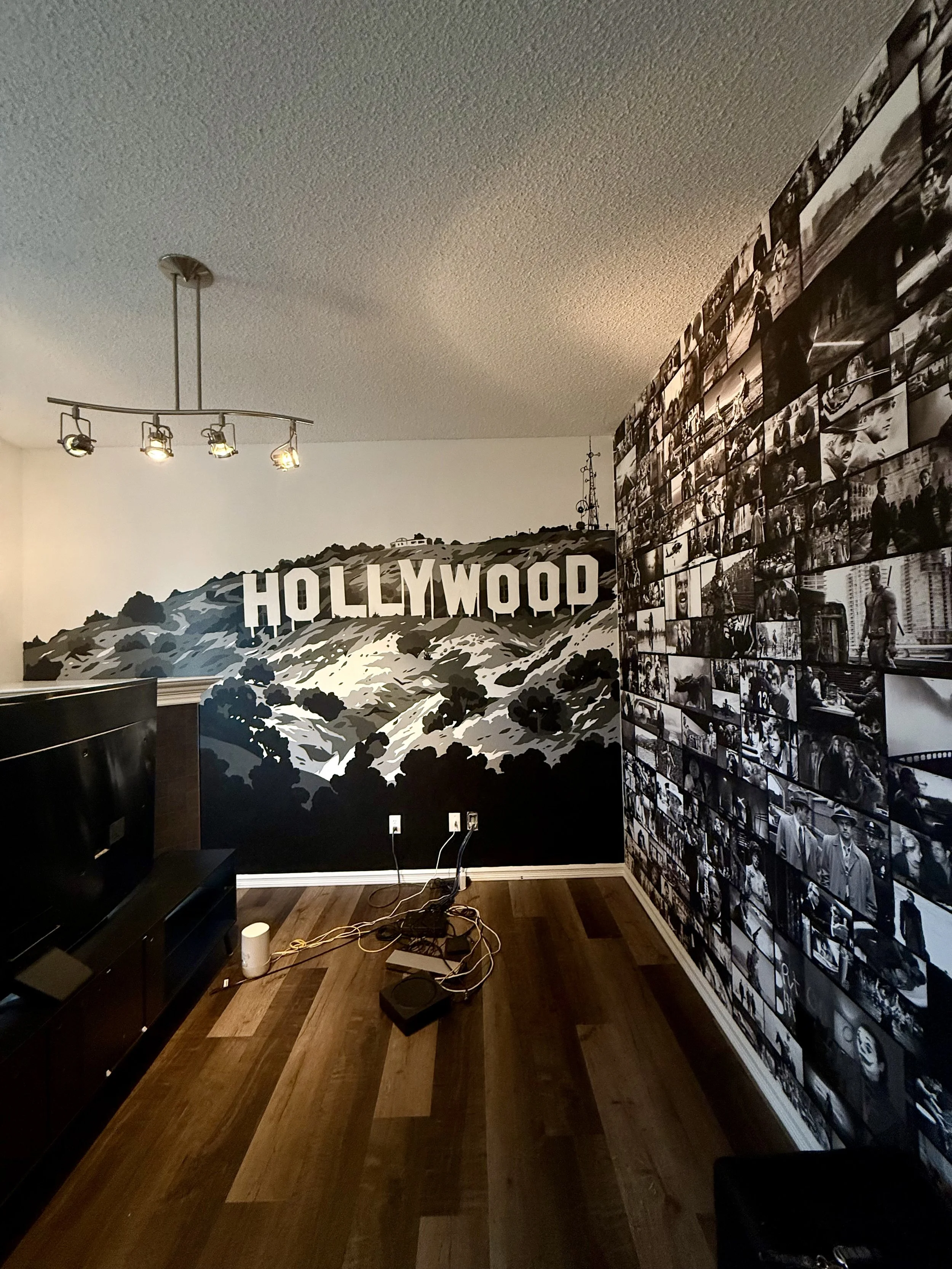 Movie room mural in residential home with a large black-and-white photo collage wall on the right, a black and white mural of Hollywood Hills with the sign on the back wall. Mural hand painted by Edmonton, AB artist Carly Marie Murals