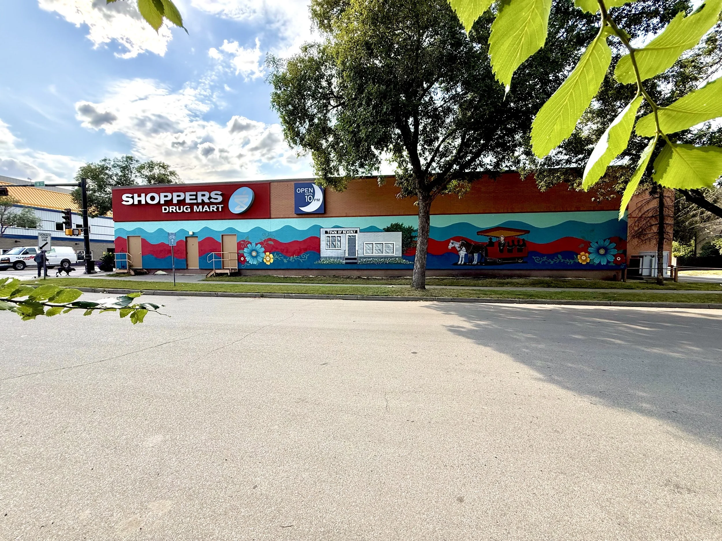 Street view of Beverly Shoppers Drug Mart mural featuring bright colours and Beverly Edmonton Historical elements Horse and Buggy, Town Hall and flowers painted by Edmonton artist Carly Marie Murals.