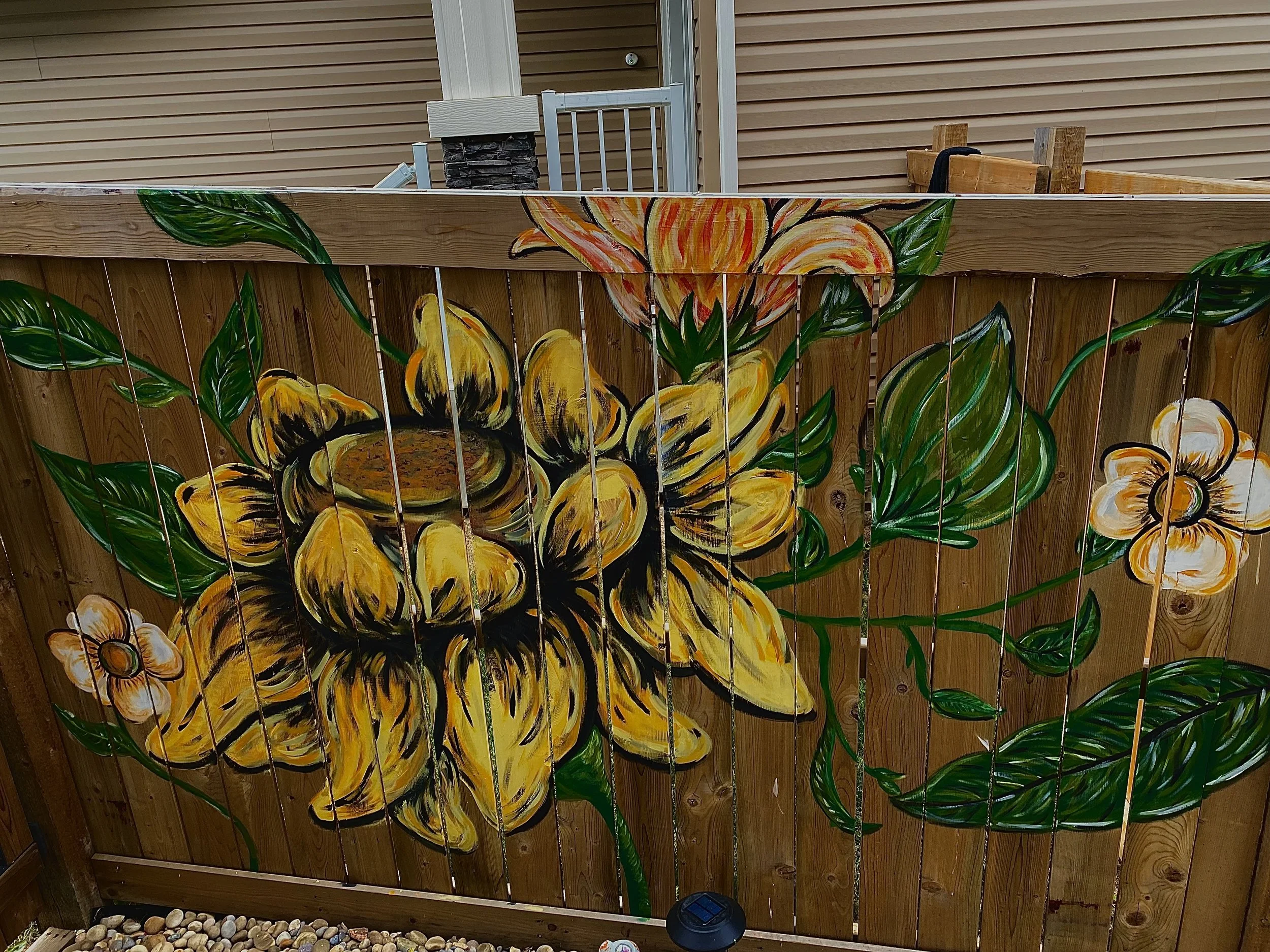 Wood fence with hand painted sunflower and leaves with orange flowers painted on it in the backyard