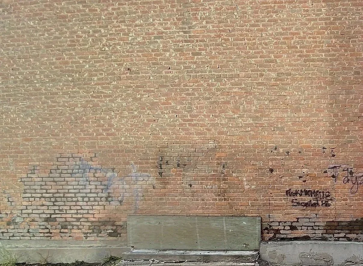 Exterior Brick wall showing visible patches, staining, and discolouration remaining after graffiti removal at Wetaskiwin Heritage Museum in Alberta