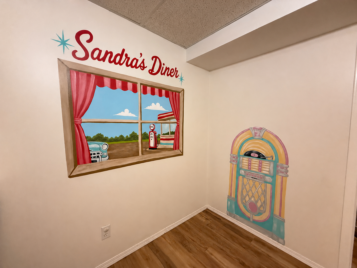50's style mural hand painted faux window with 50s scene and Sandra Diners in bold red script above it a hand painted juke box in 50s pink, yellow, and blue