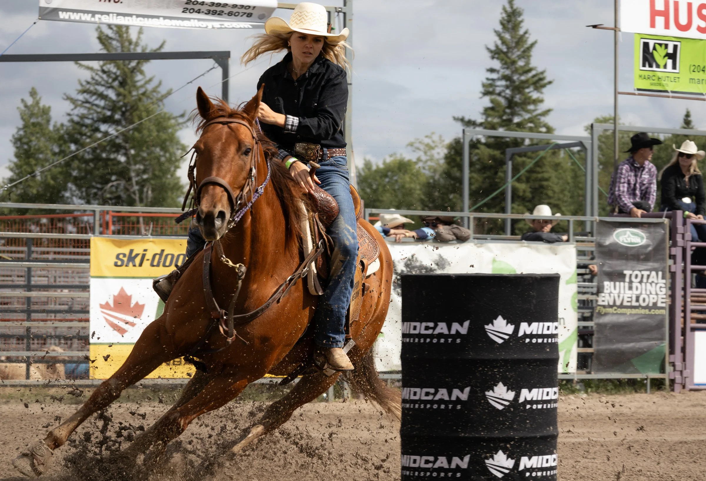 Cowgirl in hat leans forward as her horse rounds a barrel at speed in a rodeo arena, dirt flying beneath the hooves.