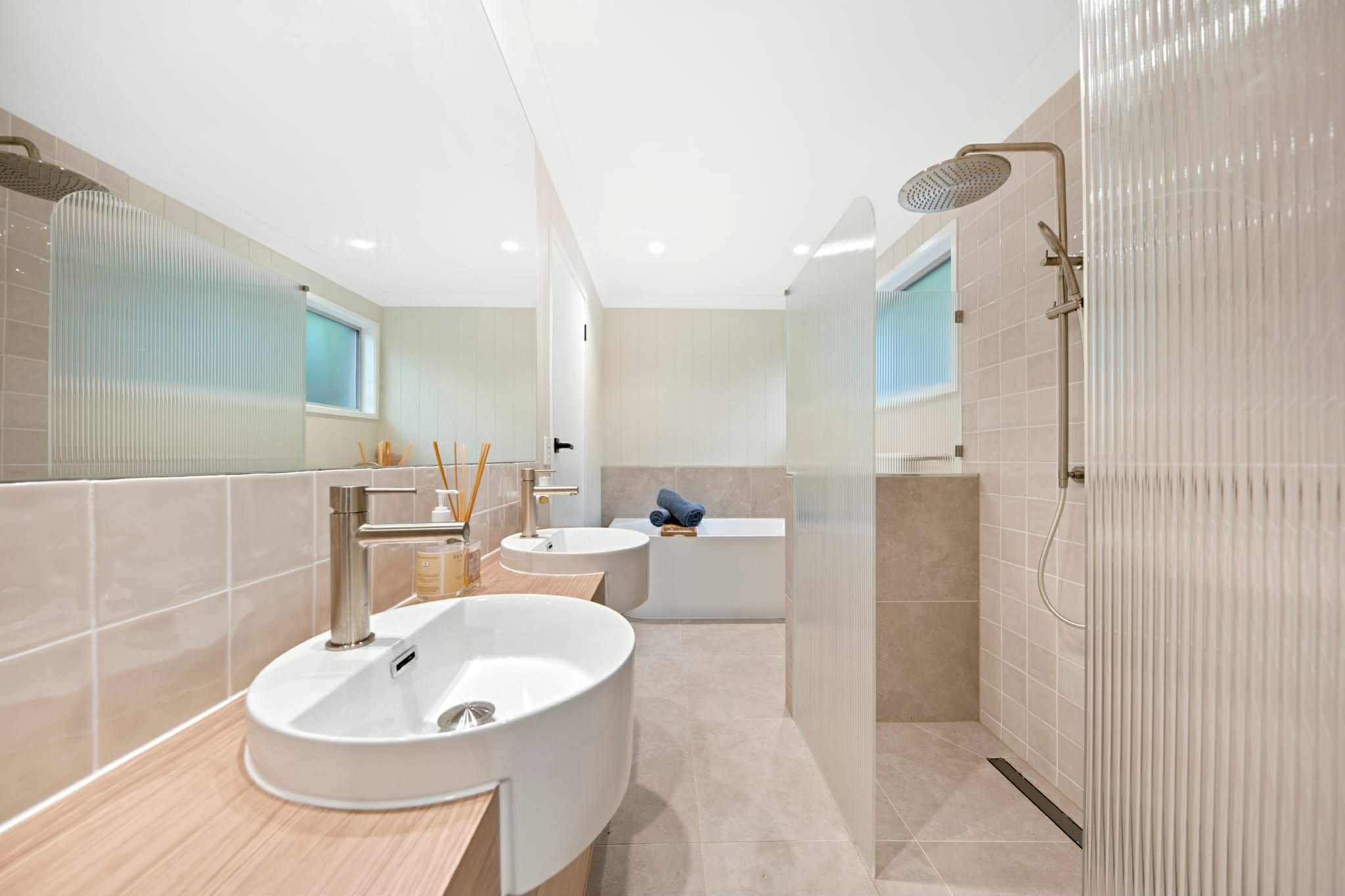 Modern bathroom with dual sinks, a bathtub with rolled towels, and a walk-in shower with a rain showerhead.