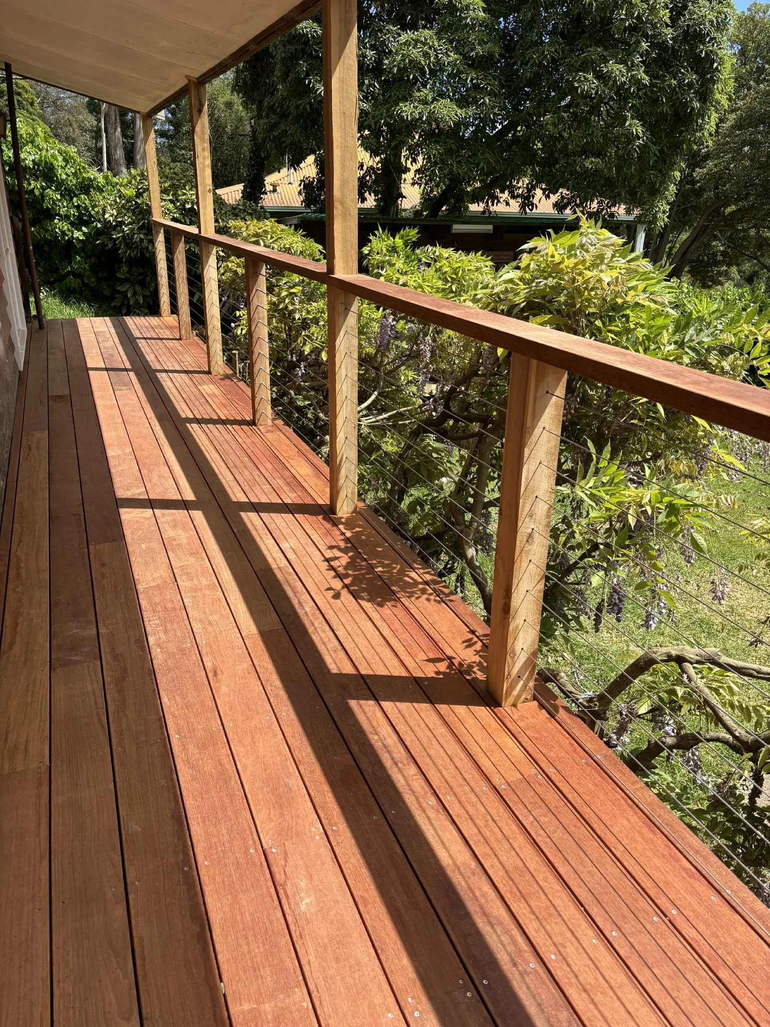 Wooden balcony with railings overlooking green trees and foliage.