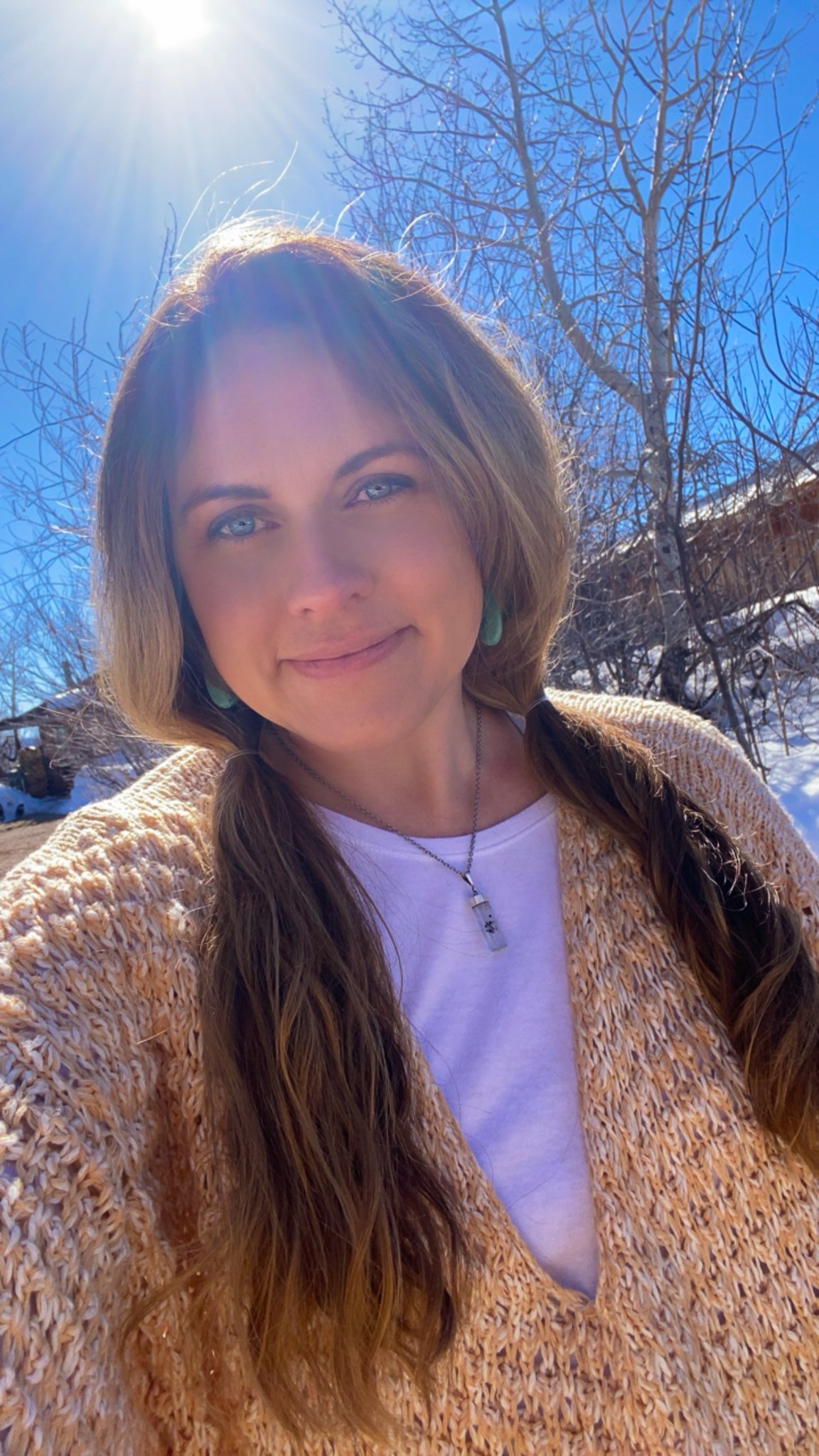 A woman with long, wavy brown hair and blue eyes outdoors on a sunny winter day.
