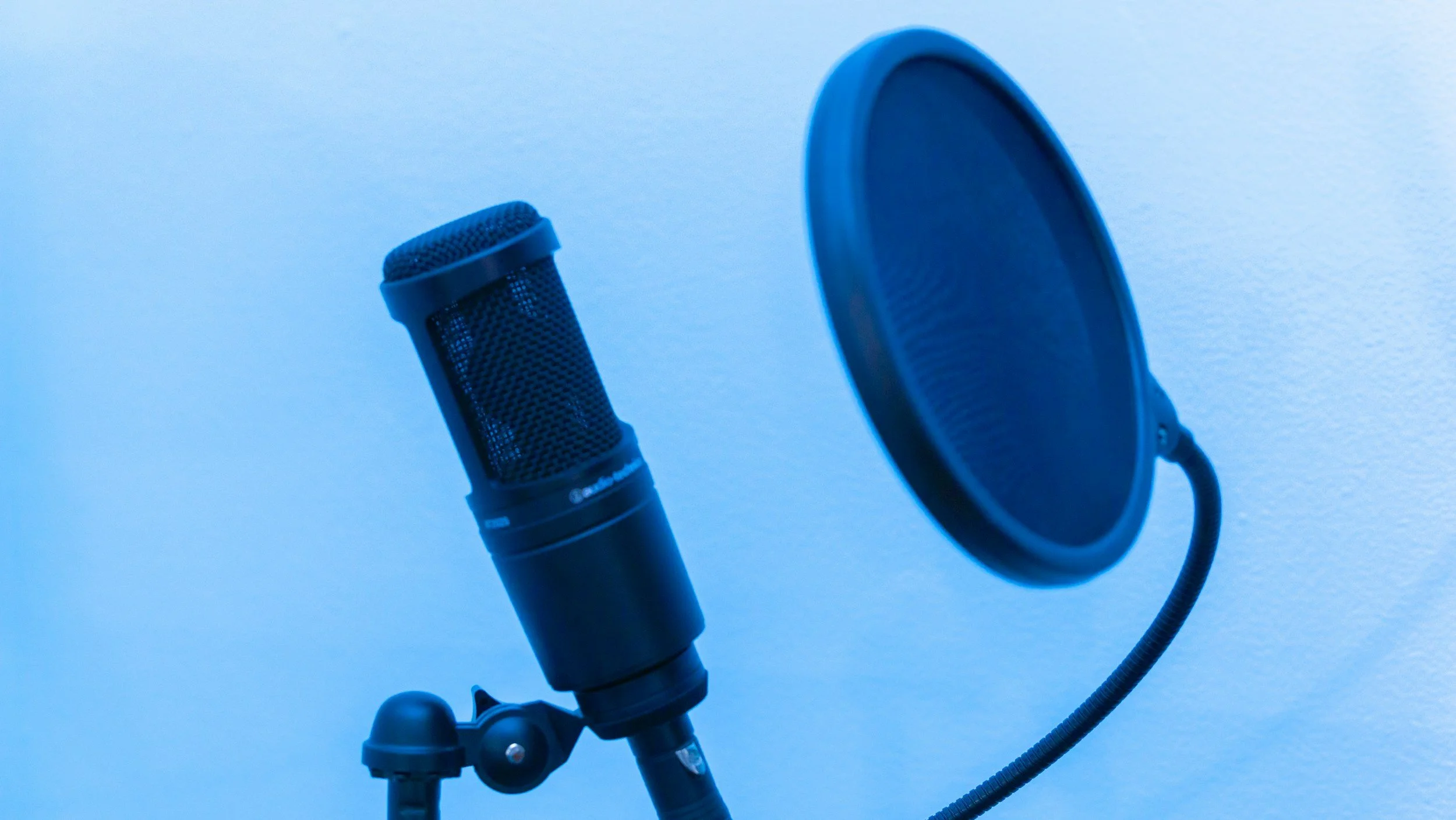 A professional microphone with a pop filter against a plain blue background.