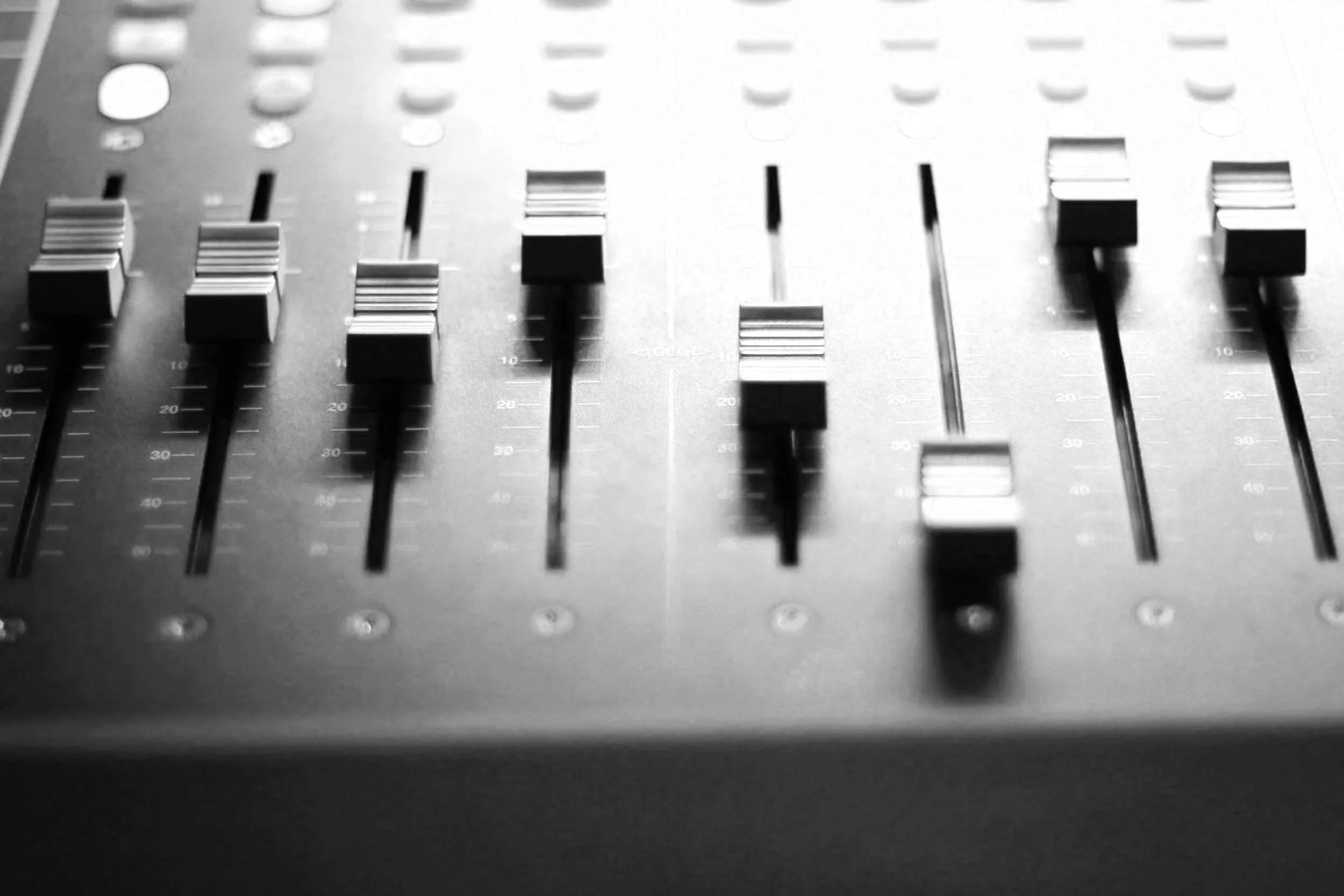 Close-up of a black and white audio mixing console with various sliders and knobs.
