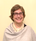 A woman with short brown hair, glasses, and a warm smile, wearing a light gray cardigan over a beige top.