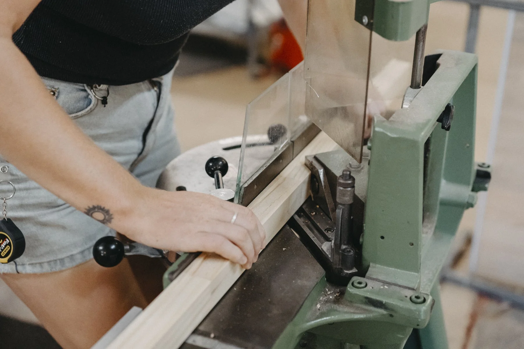 A person operating a wood planer machine, smoothing a piece of wood in a workshop.