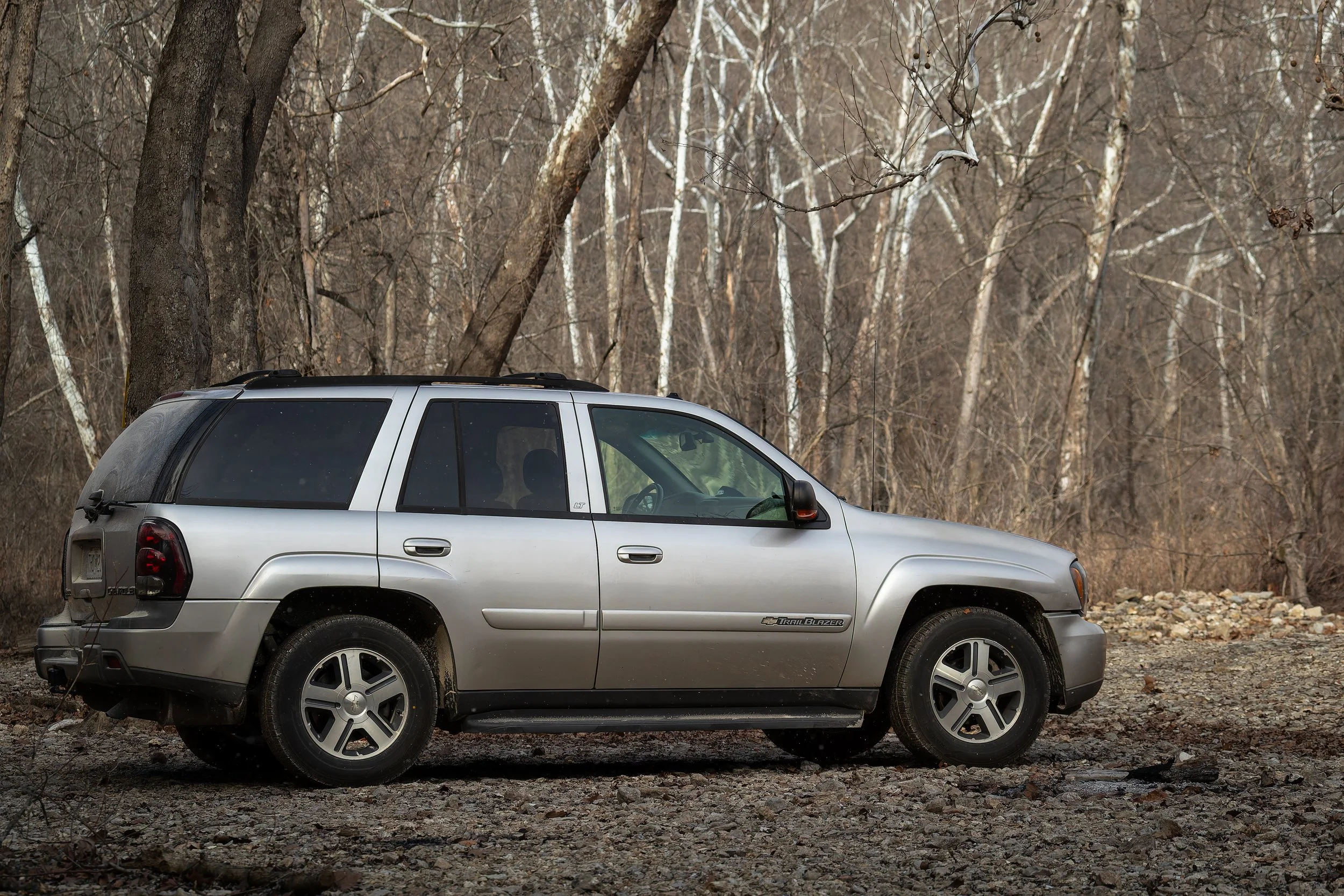 A silver SUV parked on a rocky, wooded terrain with leafless trees in the background.