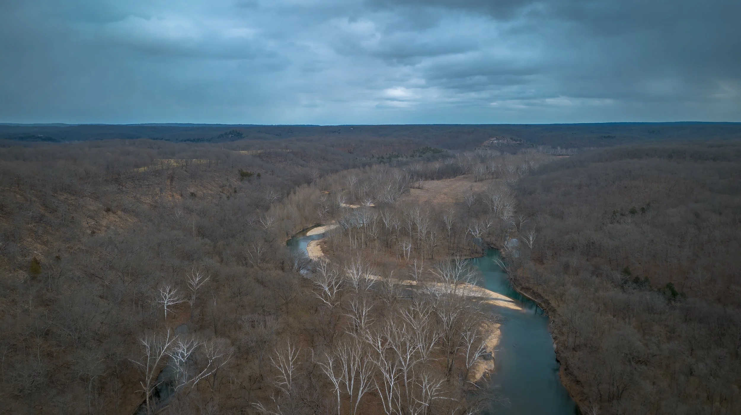 Aerial view of a winding river flowing through a forested landscape under a cloudy sky.