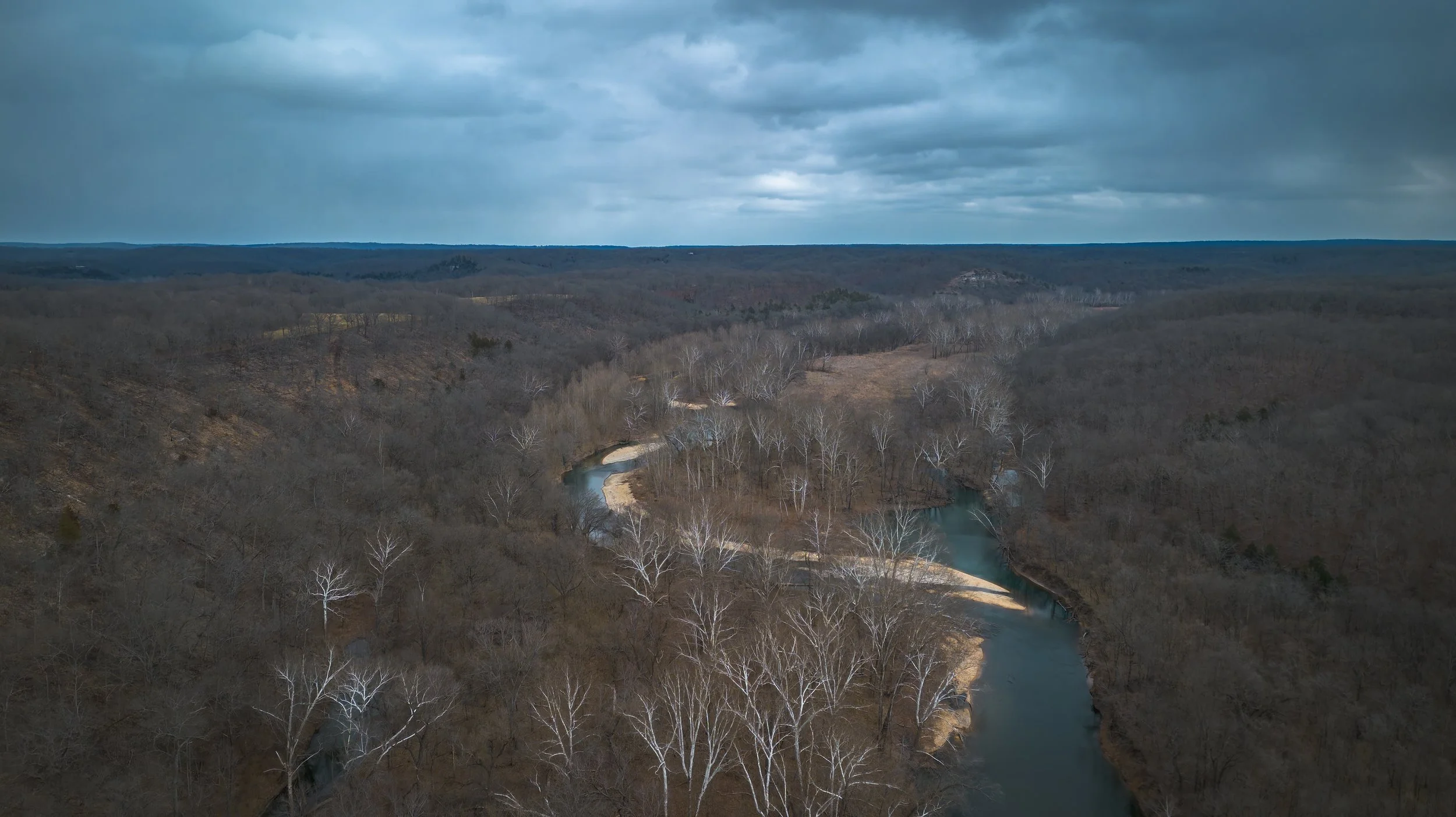 Aerial view of a winding river through a forested landscape under a cloudy sky.