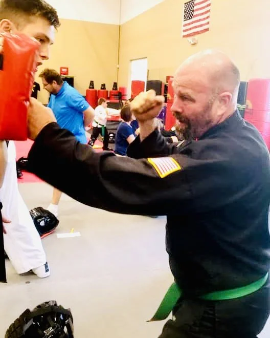 Adult student punching a hand pad in a martial arts and self-defense class at Karate John's Martial Arts center in Cicero and Liverpool, NY.