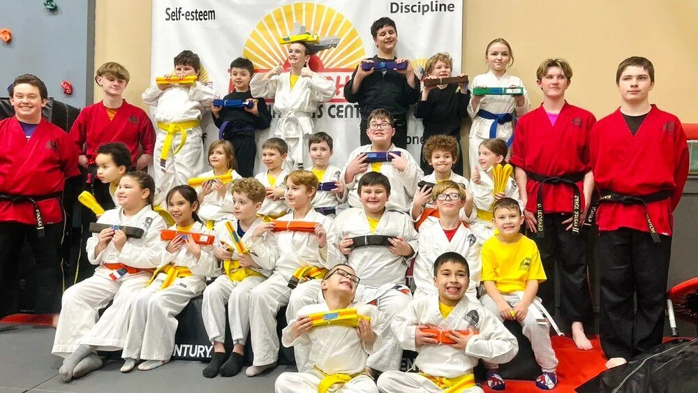Kids and teens celebrating karate belt promotions at Karate John’s Martial Arts Center in Cicero and Liverpool, NY after completing martial arts training that develops confidence, discipline, leadership and self-defense skills.