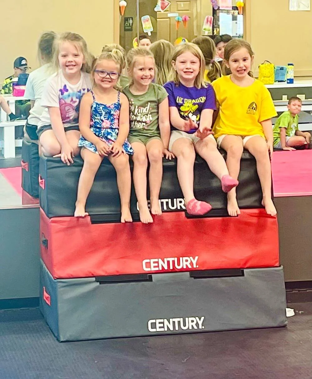 Group of smiling girls sitting on a bench and having fun at Karate John's summer camp in Cicero, NY.