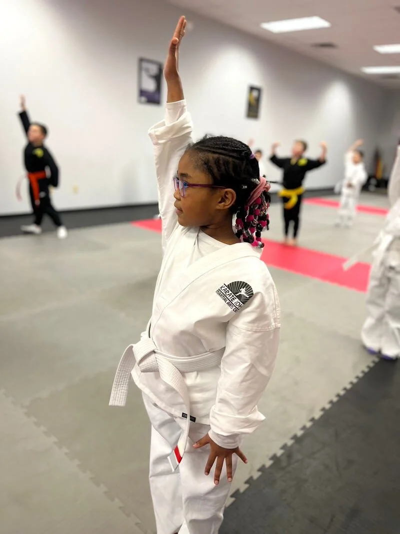 Girl standing tall raising her hands with confidence at Karate John's summer camp in Cicero, NY.