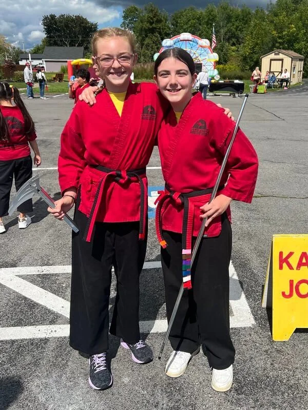 Two teen girls holding martial arts weapons and practicing in front of Karate John's Martial Arts Centers in Cicero and Liverpool, NY.