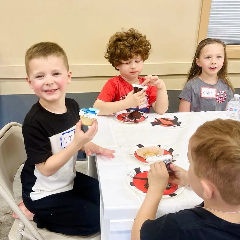 Smiling kids sitting at a table eating birthday party cupcakes at Karate John's Martial Arts.