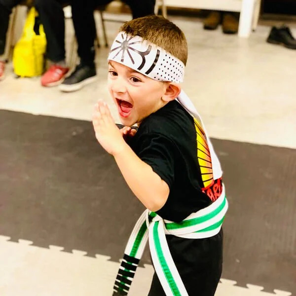 Smiling child getting ready to break a karate birthday board with a chop at Karate John's Martial Arts in Cicero and Liverpool, NY.