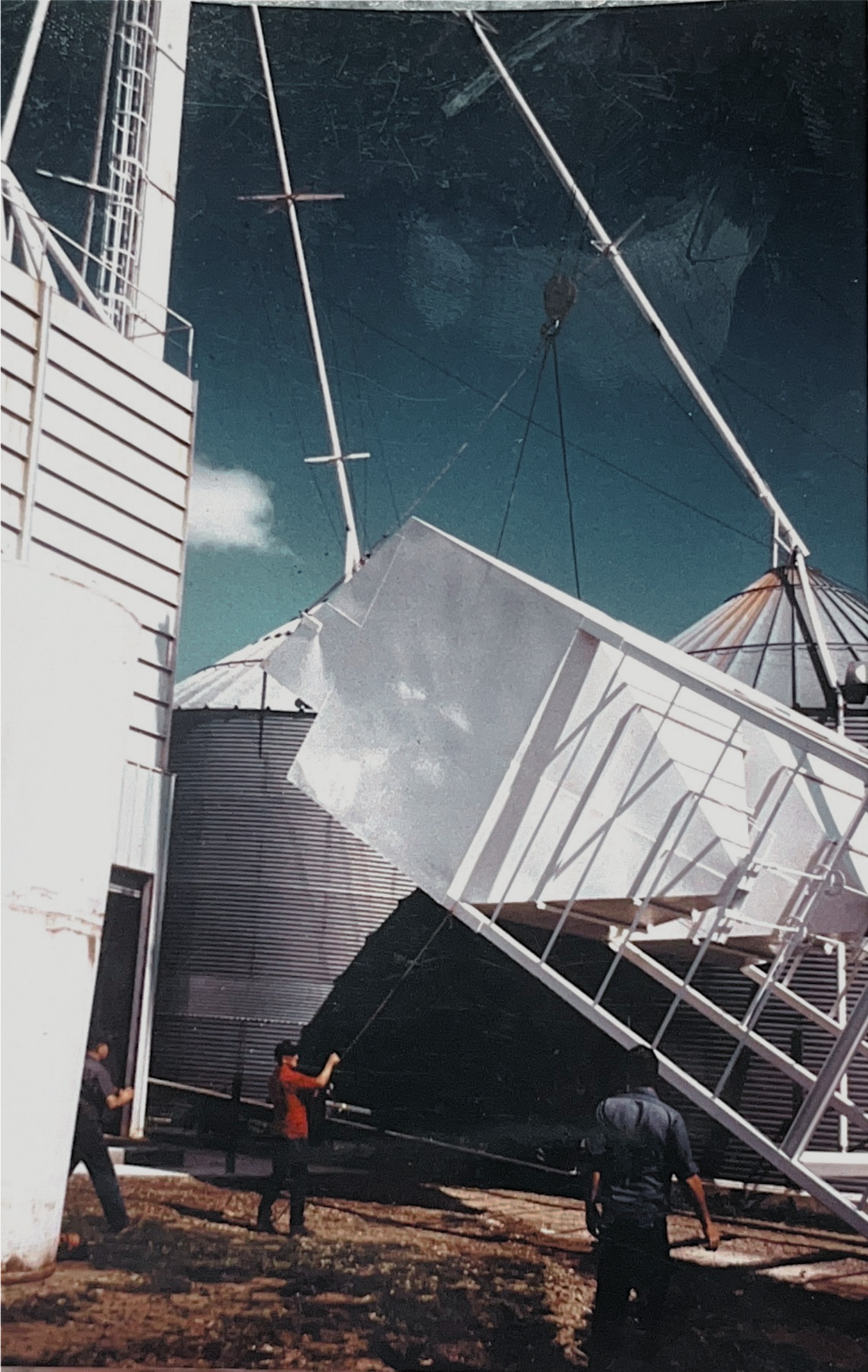 People working to stabilize or assemble large, tilted metallic structures outdoors at a construction site.