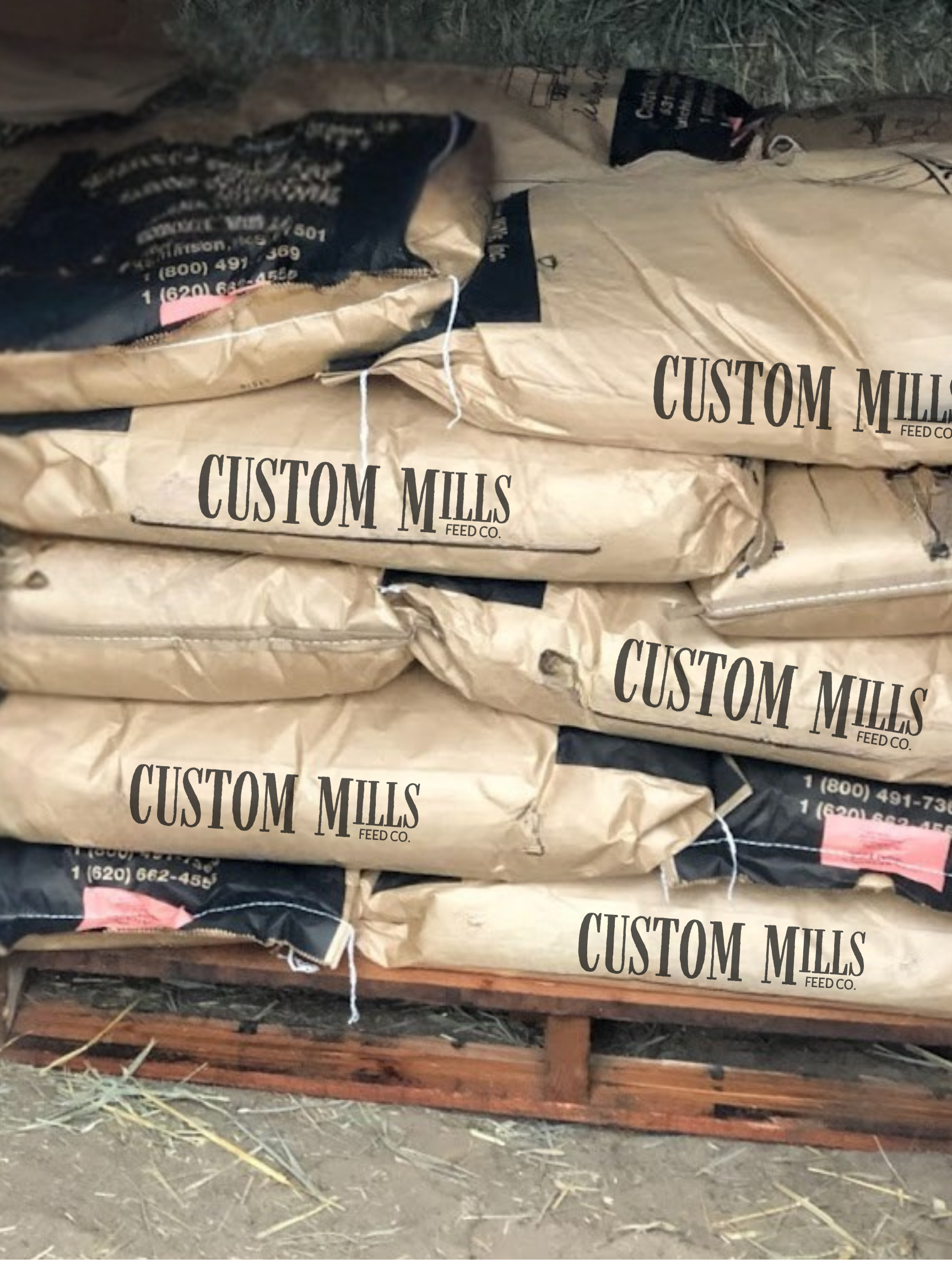Stack of beige and dark blue feed bags labeled 'Custom Mills Feed Co.' and various numbers, on a wooden pallet.
