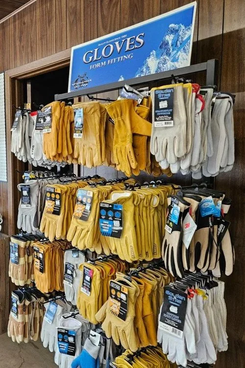 Display of winter gloves in various colors and styles on hooks under a sign that reads "GLOVES FOR HITTING."