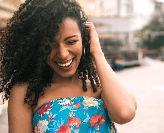 BIPOC woman smiling as she pushes hair behind left ear