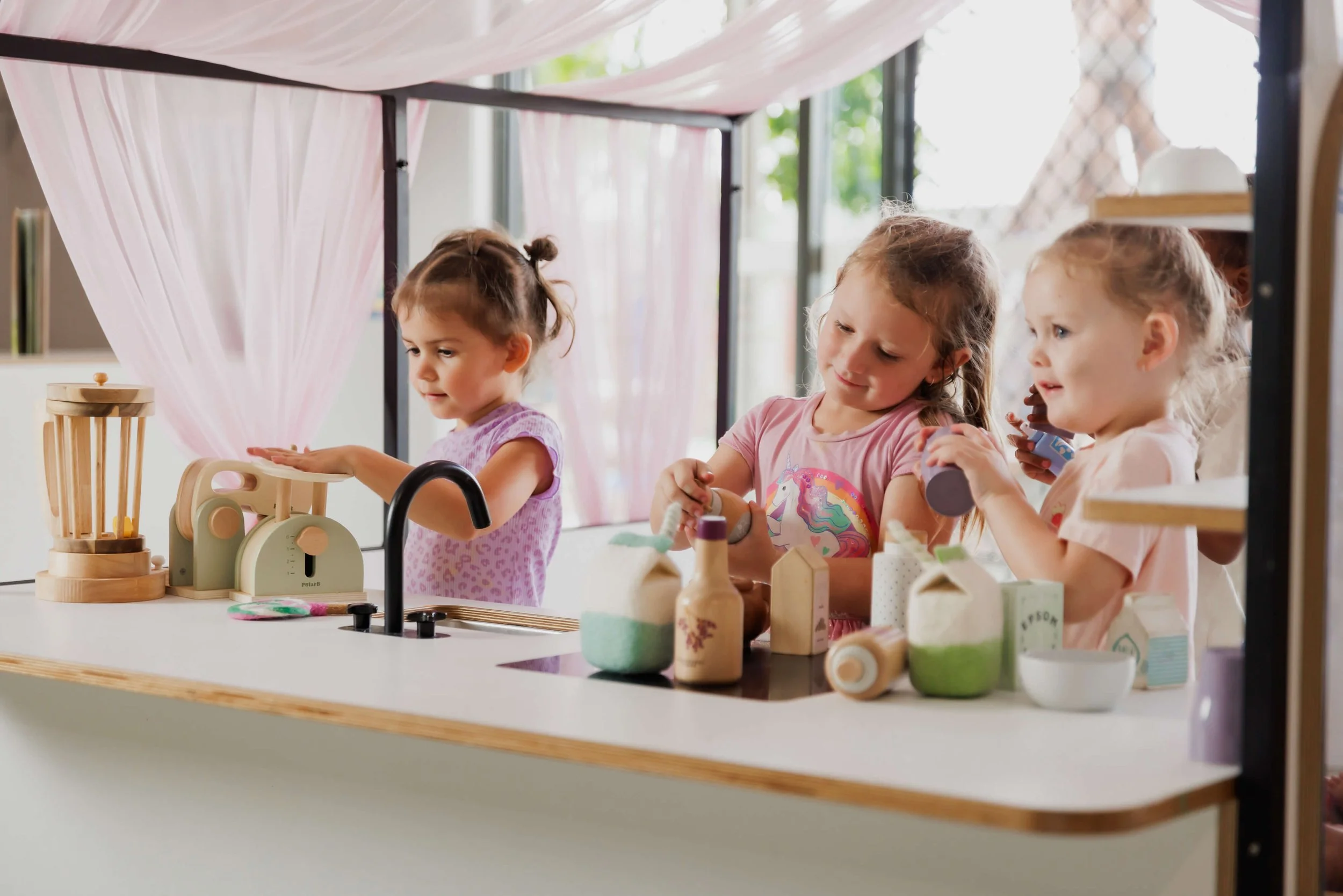 Three young girls playing pretend with toys.