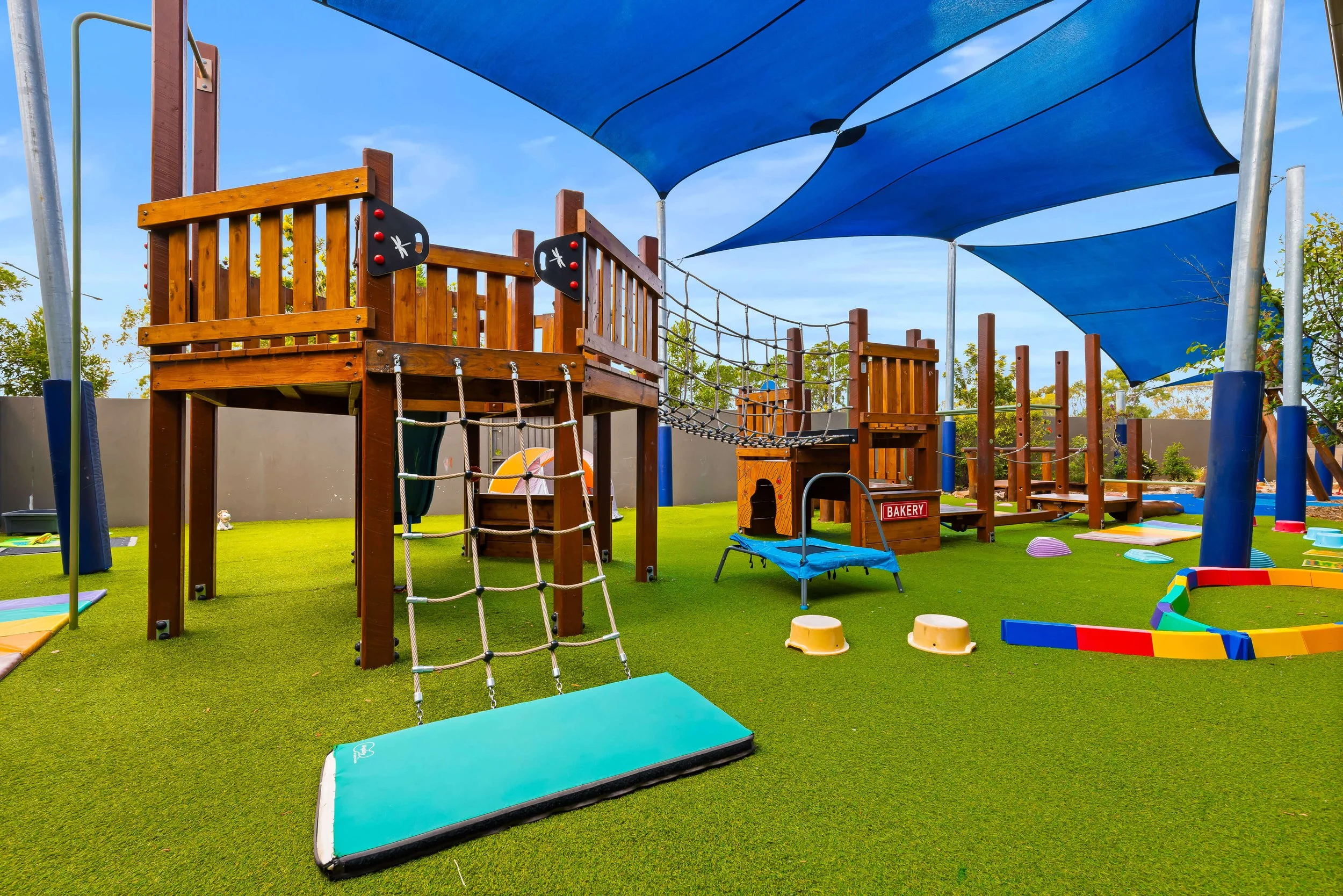 A welcoming outdoor playground with green grass and blue sun shades.