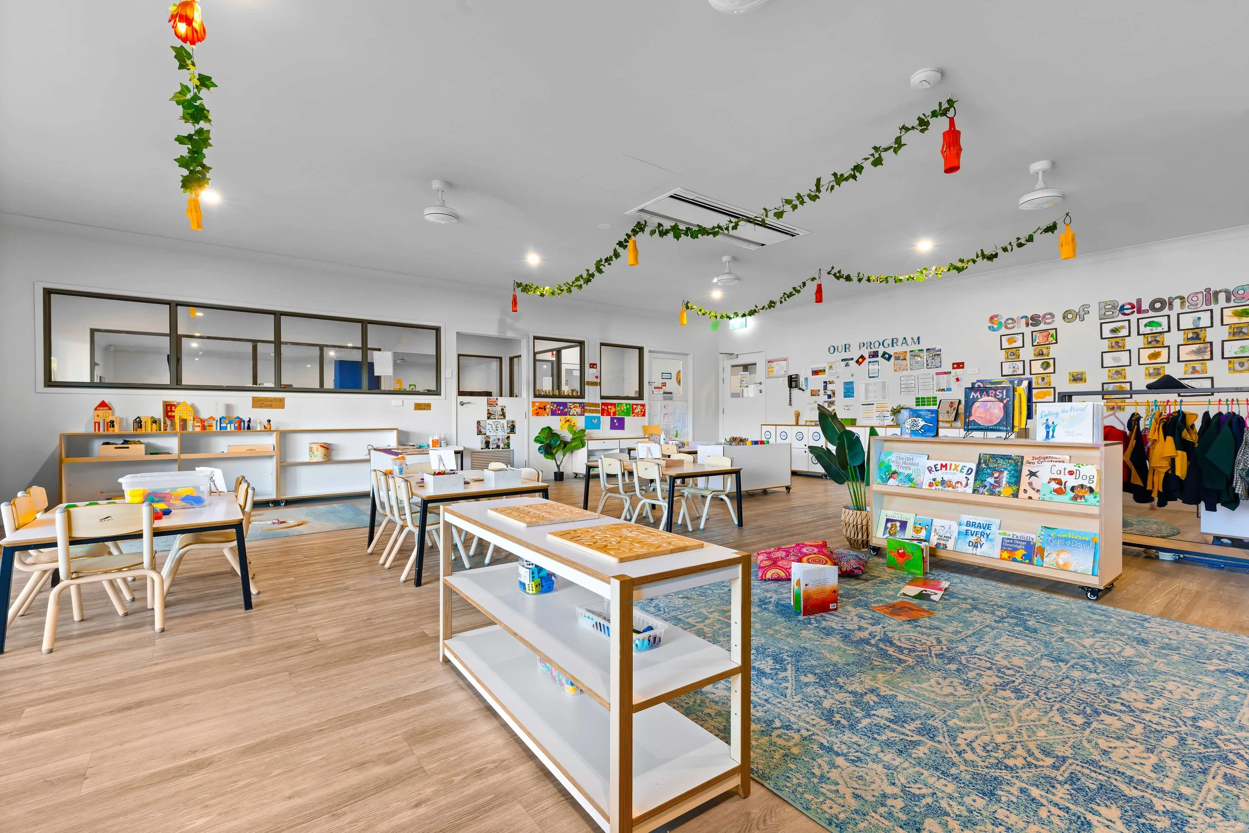 A wide shot of a clean and modern interior of a childcare centre with tables and chairs and colourful decorations.