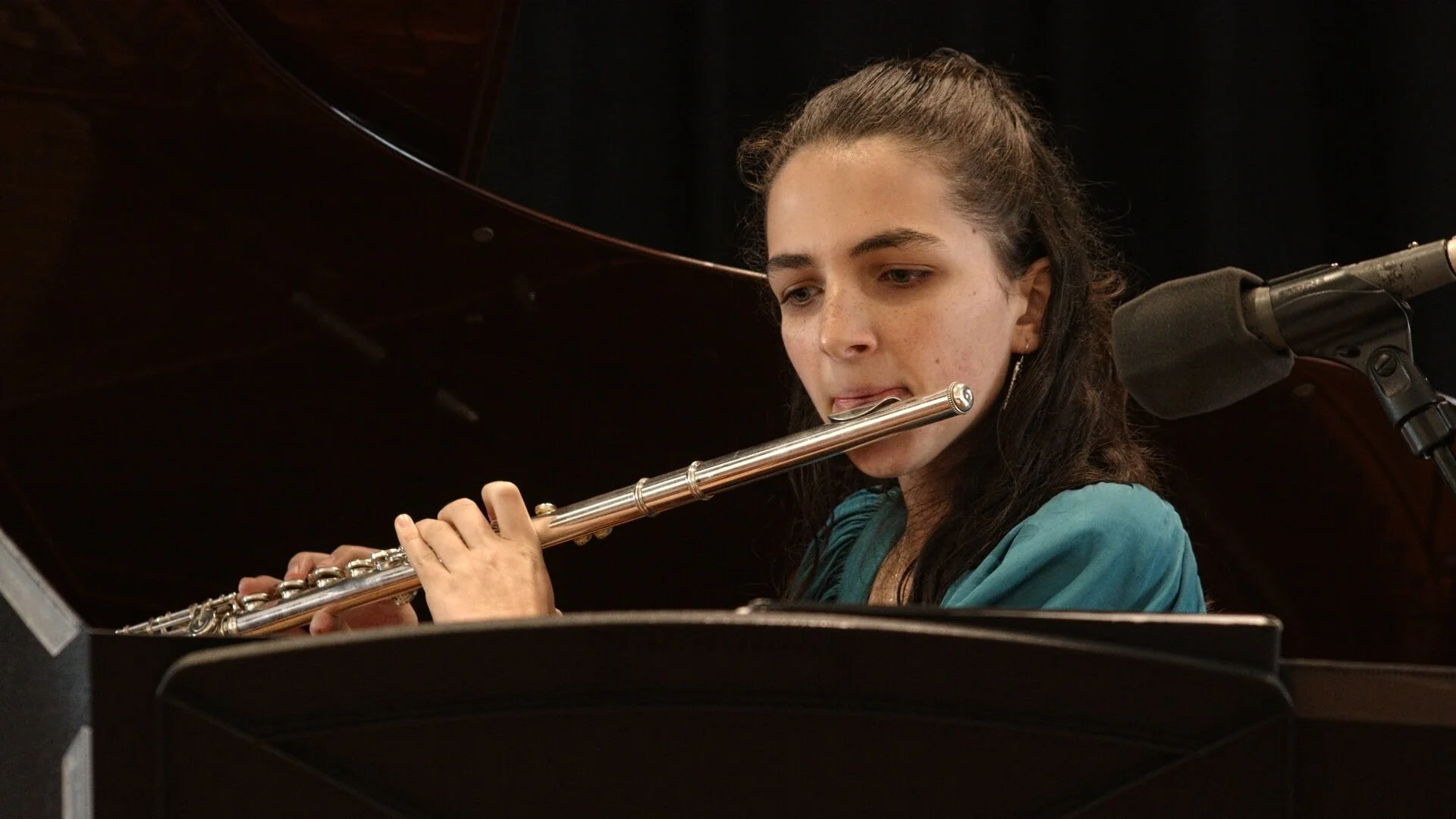 Young woman playing the flute during a musical performance, with a black background and music stand in front.