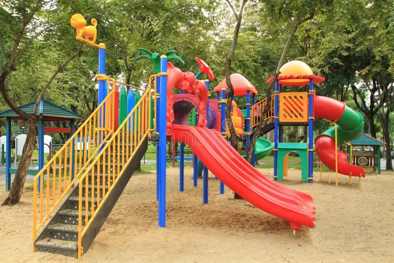 Colorful playground with slides and climbing structures in a park surrounded by trees.