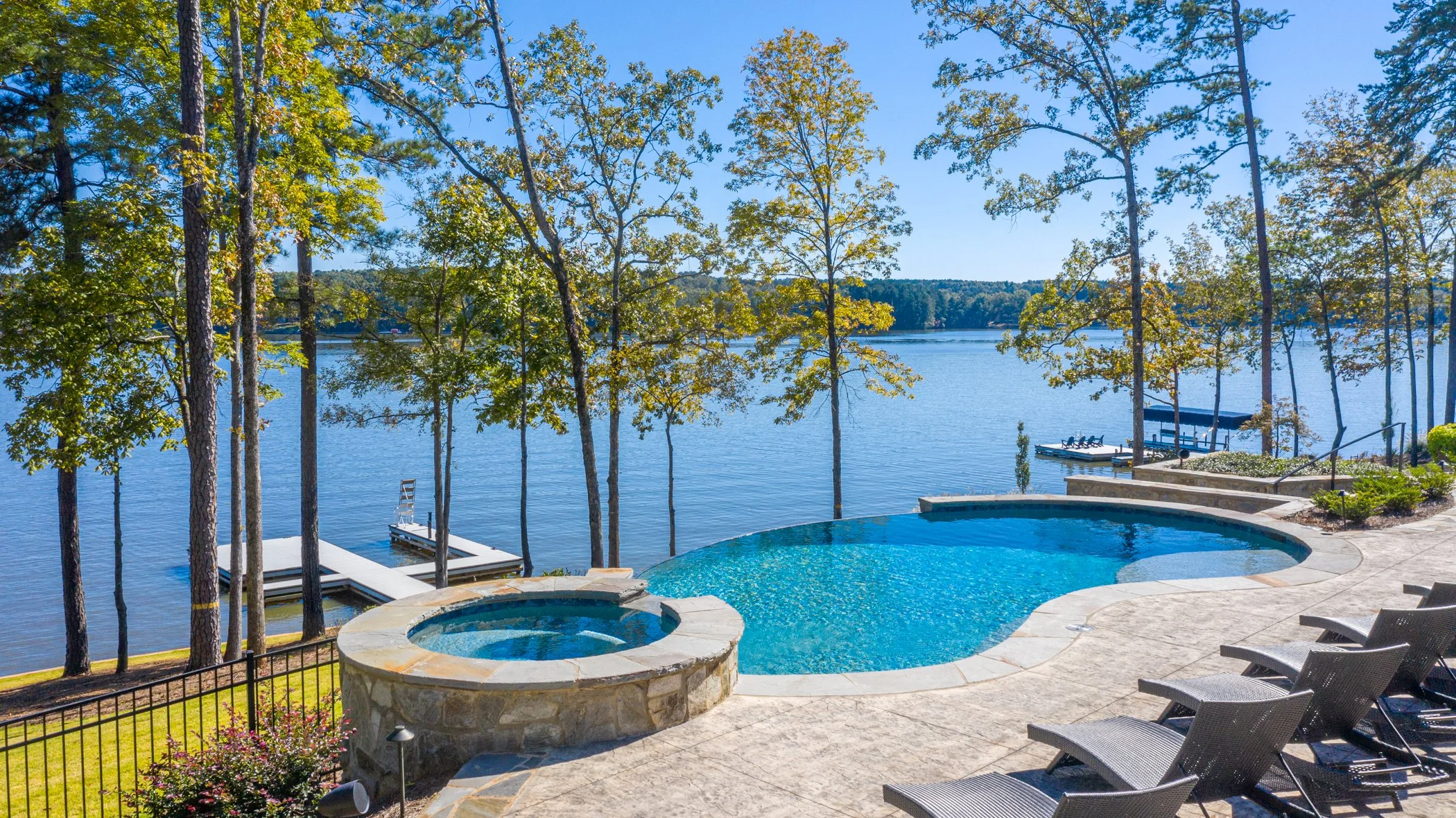 Luxury backyard with a swimming pool and hot tub overlooking a lake with trees and a dock