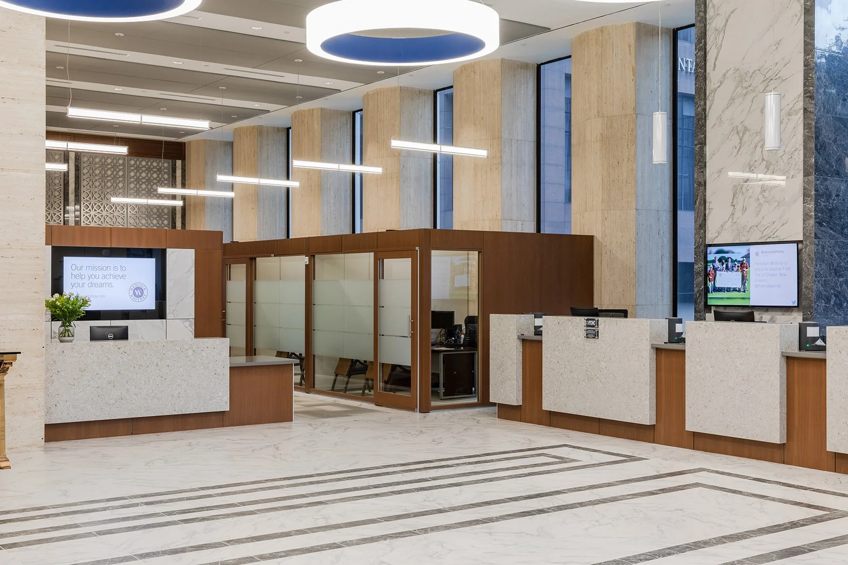 Modern lobby with check-in counters, digital screens, wood and marble decor, and large windows.