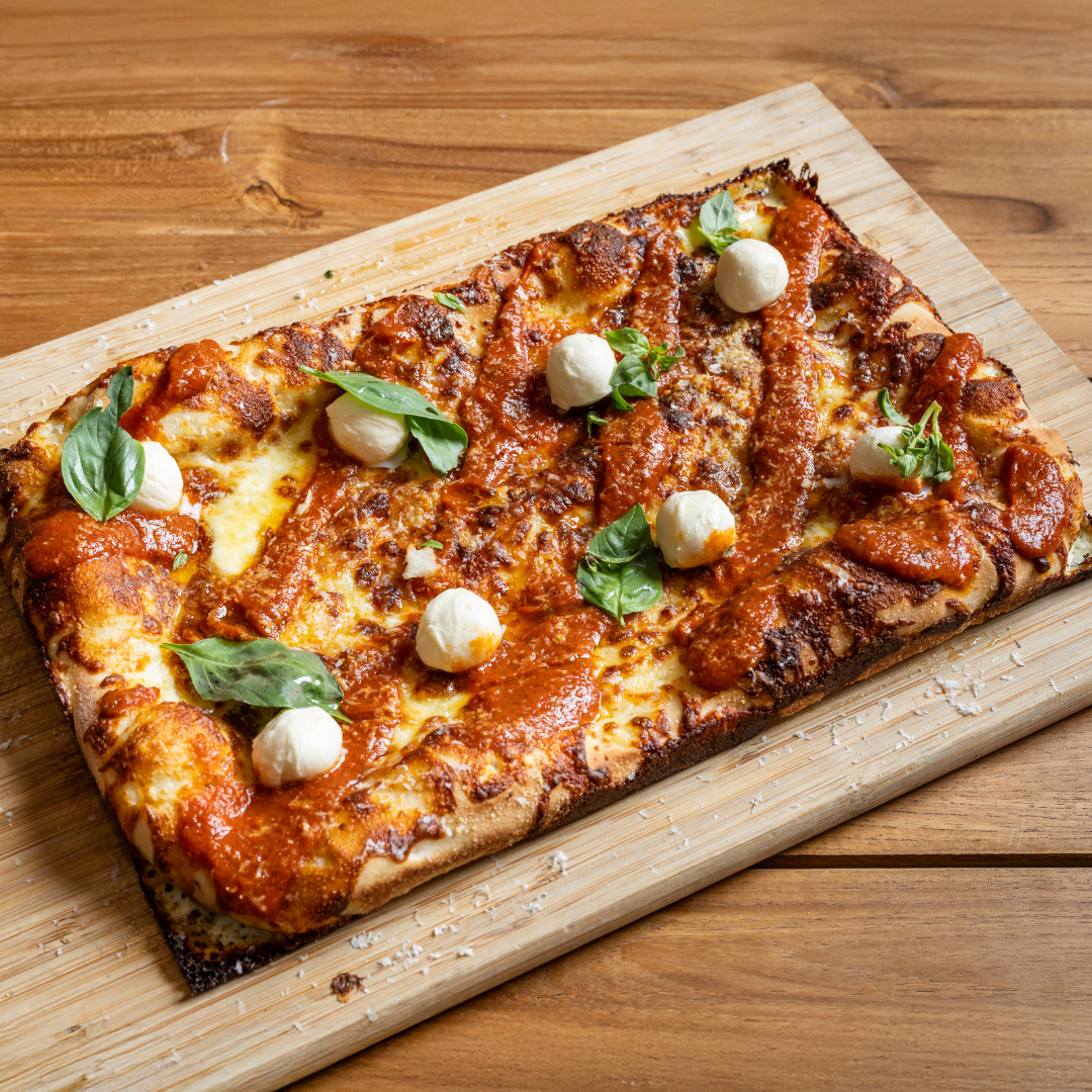 9MILE Detroit Style Square Pizza with tomato sauce, melted cheese, small mozzarella balls, fresh basil leaves, and a drizzle of sauce on a wooden cutting board.