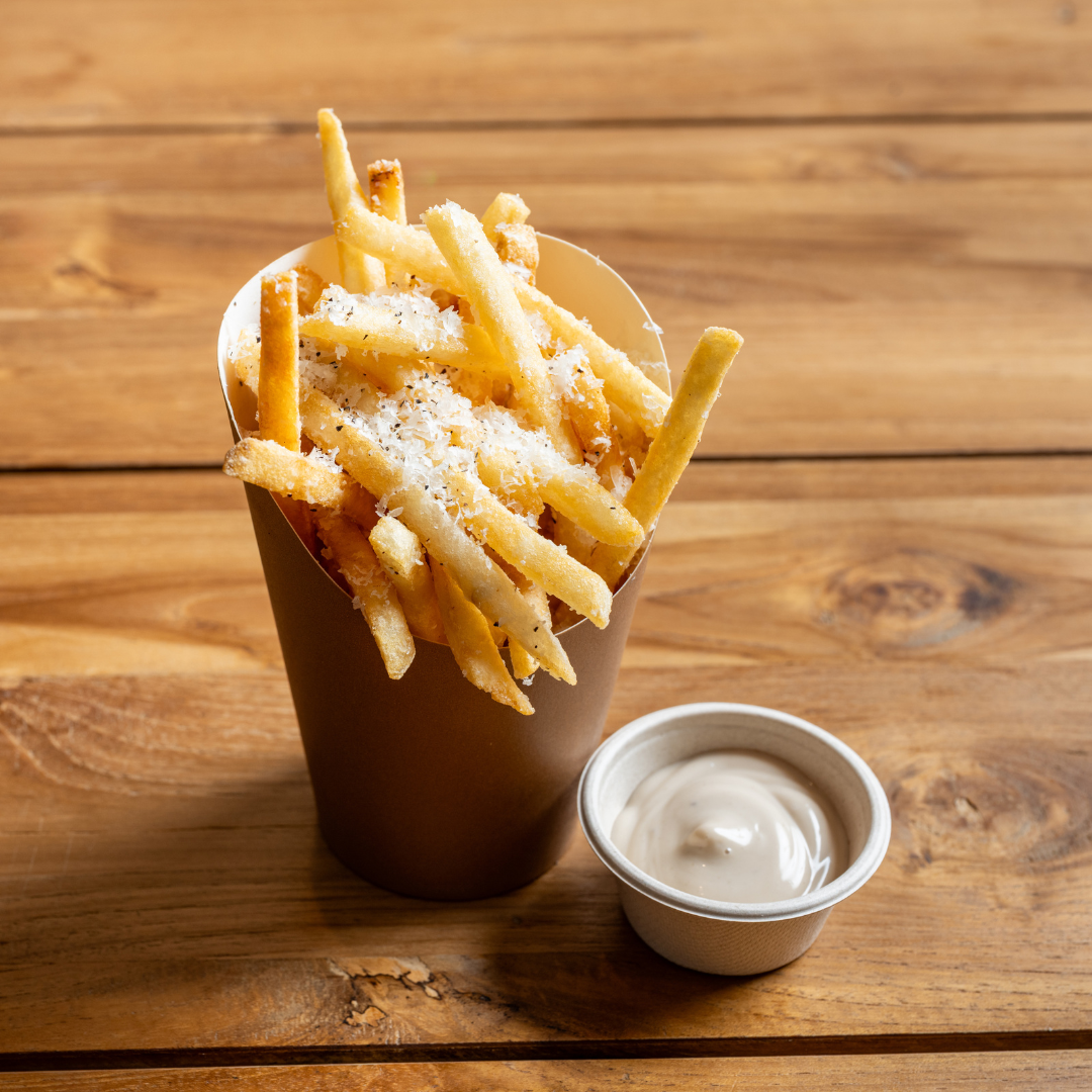 A container of 9MILE fries topped with grated cheese accompanied by a side of dipping sauce on a wooden table.