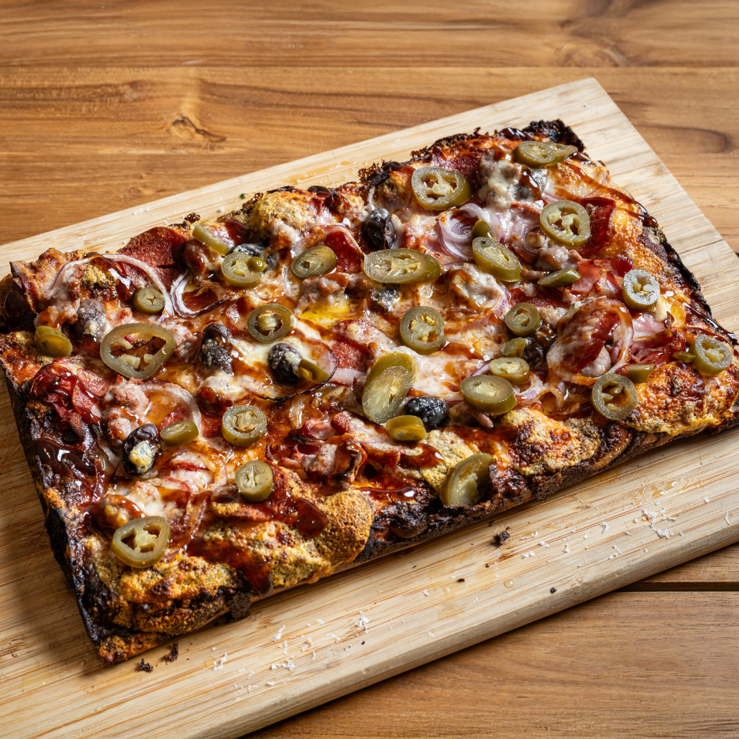 9MILE Detroit Style Square Pizza with cheese, pepperoni, black olives, green peppers, and onions on a wooden cutting board.