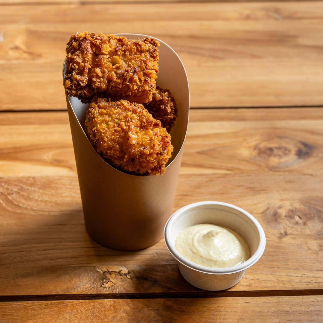 Three pieces of 9MILE fried mac and cheese in a brown paper sleeve with a small container of dipping sauce on a wooden table.