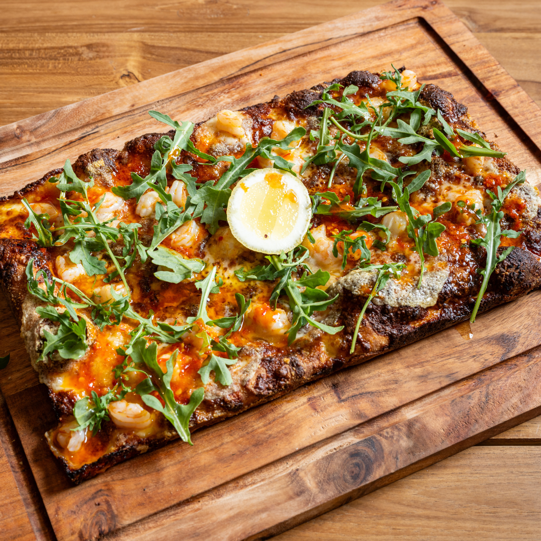 A rectangular 9MILE Detroit Style Pizza with cheese, shrimp, arugula, and a lemon slice on top, served on a wooden board.