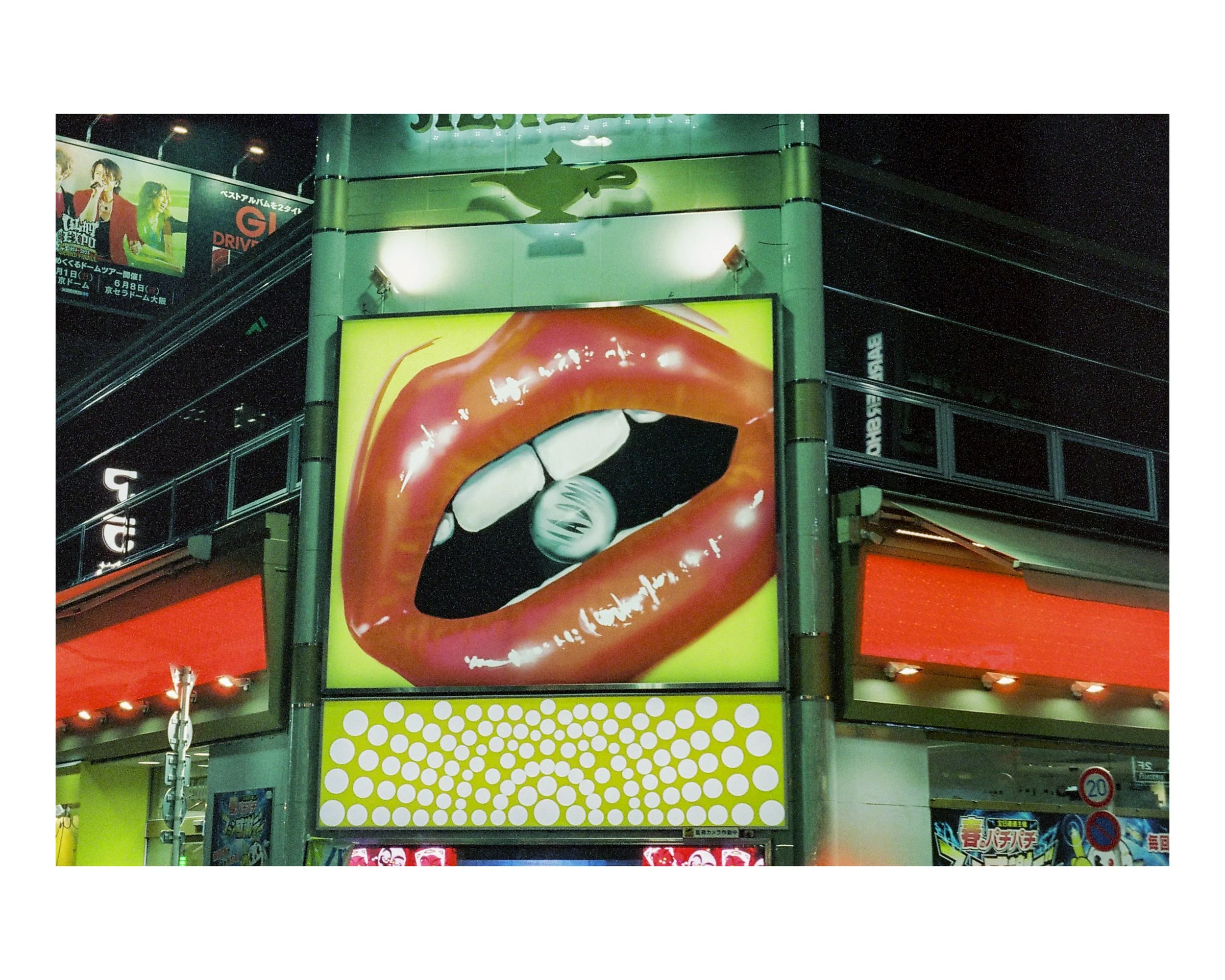 Large billboard displaying a close-up of glossy red lips biting a ball with black and white stripes, set against a bright yellow background.