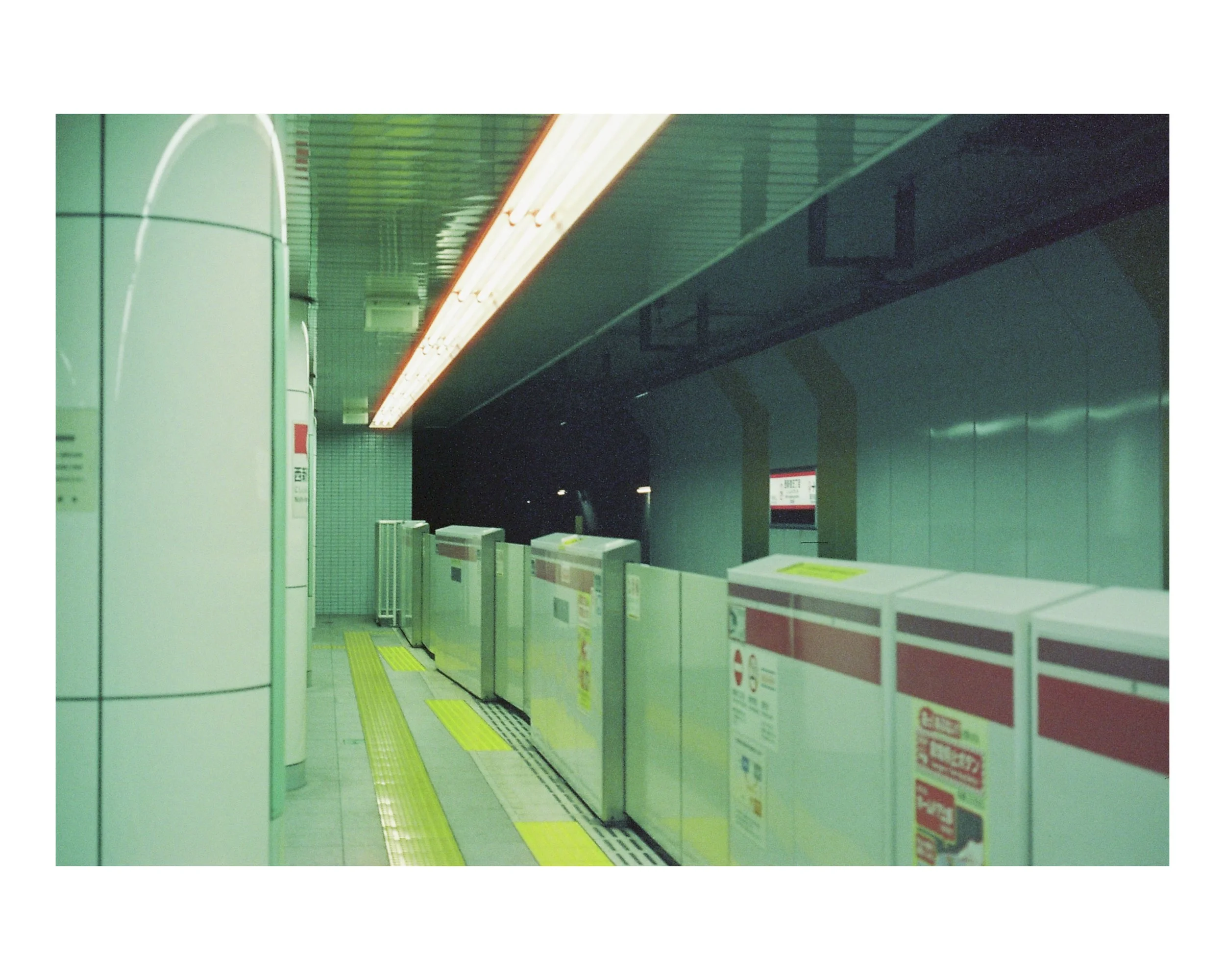 Empty subway station with ticket gates, yellow tactile paving, illuminated ceiling, and dark background beyond platform.